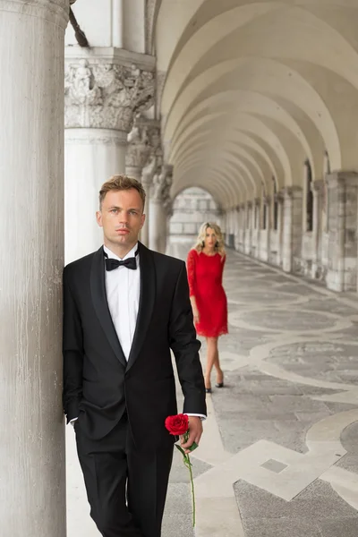 Elegantly dressed man holding rose in hand and waiting for his date — Stock Photo, Image