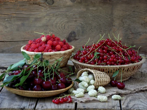 Färsk frukt och bär i korgar på trä bakgrund — Stockfoto