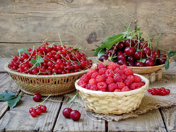 Frisches Obst und Beeren in Körben auf Holzgrund - rote Johannisbeeren, Himbeeren, Kirschen — Stockfoto