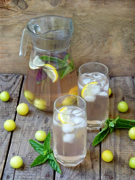 Frischer Saft oder Kompott mit Eiswürfeln und einer Zitronenscheibe mit einer gelben Pflaume und Basilikum — Stockfoto