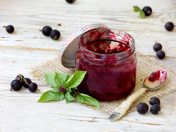 Een potje jam van de zwarte bes op een houten achtergrond — Stockfoto