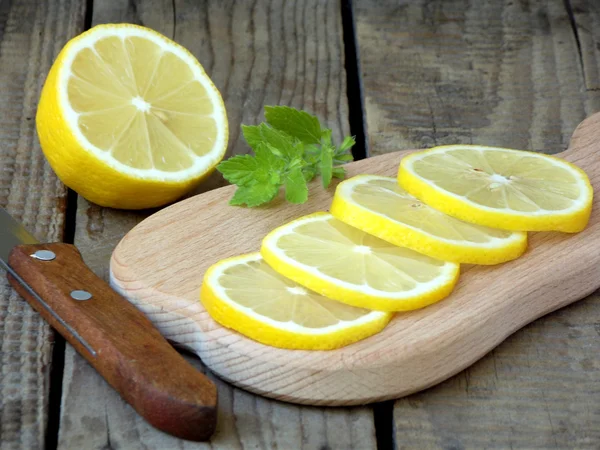 Gehackte Zitronenscheiben auf einem Holzbrett, ein Messer und ein Zweig Minze — Stockfoto