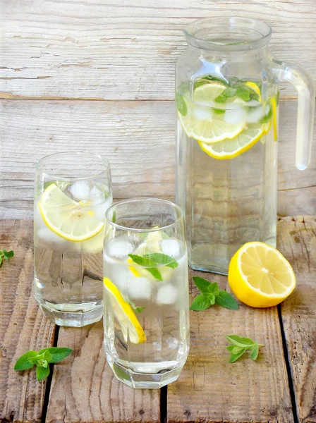 Два больших стакана холодного лимонада со льдом, лимоном, листьями мяты и соломой . — стоковое фото