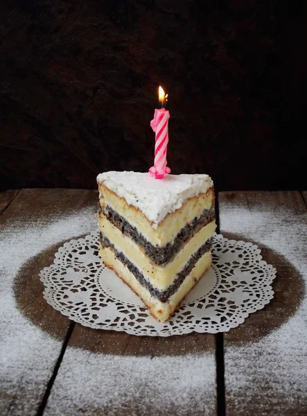 Piece of lemon poppy seed cake with curd cream and pink burning candle on a dark wooden background. selective focus. birthday cake — Stock Photo, Image