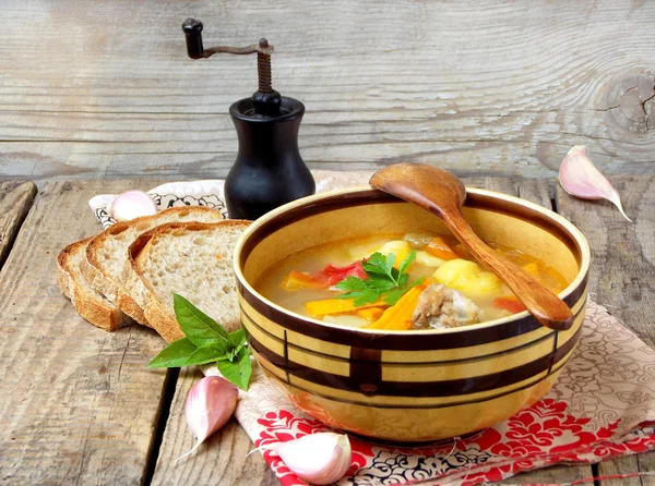 Bowl of soup with potatoes, carrots, sweet peppers and tomatoes on a wooden background. selective focus — Stock Photo, Image