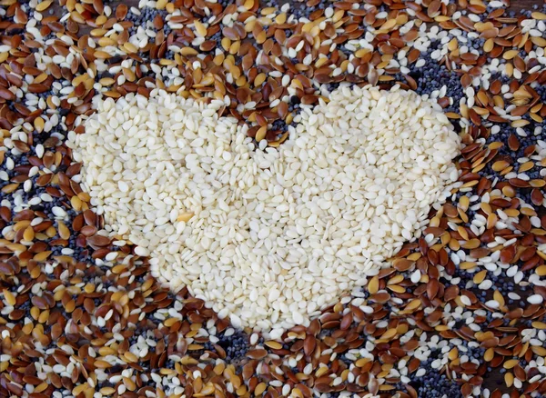 Corazón de sésamo blanco sobre fondo de diferentes semillas. enfoque selectivo — Foto de Stock