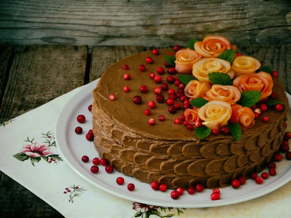 Gâteau au chocolat avec des roses faites de pommes et de canneberges sur un fond en bois — Photo