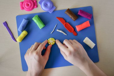 Çocuklar için plasticine lolipop modellemesi yedinci adımda yatıyordu. Küçük detaylar ve çubuk ve el yapımı tatlılar ekliyordu. Yaratıcı beceriler öğreniyordu.