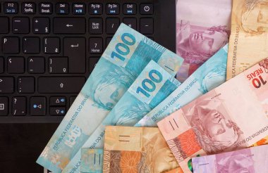 Dizüstü bilgisayarın üstüne gerçek Brezilya banknotları. Brezilya parası işte. Çevrimiçi alışveriş kavramı. 