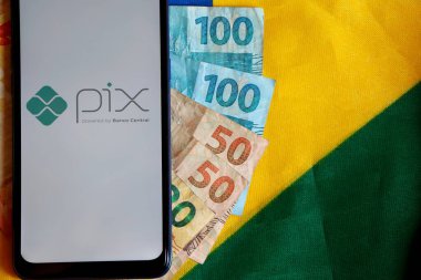 Brezilya - 9 Ekim 2020. PIX - akıllı telefon ekranında Banco Central ve Brezilya bayrağının tepesinde Brezilya Real banknotları. Pix, Brezilya Merkez Bankası 'nın yeni acil ödeme sistemi..