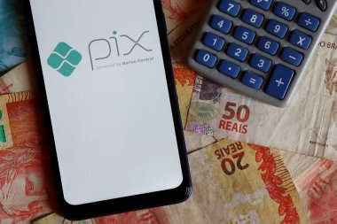 Brezilya - 9 Ekim 2020. Akıllı telefon ekranında PIX logosu ve Brezilya Real banknotlarının üstünde hesap makinesi. Pix, Brezilya Merkez Bankası 'nın yeni acil ödeme sistemi..