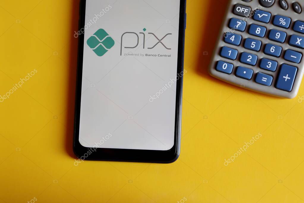 Bahia, Brazil - October 9, 2020. Pix logo on smartphone screen and calculator on yellow background. Pix is the new instant payment system from Central Bank of Brazil (Banco Central do Brasil).