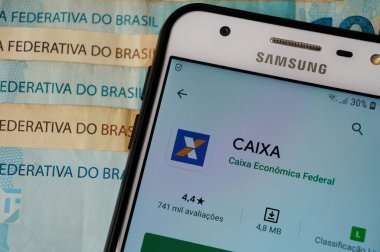 Bahia, Brezilya. 23 Nisan 2020. Caixa uygulamasını Brezilya Real banknotlarının üstünde akıllı telefon ekranına koy. Caixa bir Brezilya bankası. Caixa Bankası (Banco Caixa Economica).