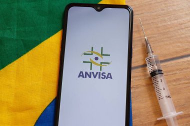 Bahia, Brezilya - 23 Mart 2021. Akıllı telefon ekranında anvize logosu ve Brezilya bayrağının tepesinde şırınga. Brezilya aşısı konsepti. Covid 19.