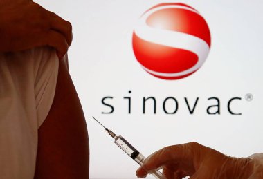 Bahia, Brazil - December 23, 2020: Nurse holding a syringe against woman's shoulder, with Chinese Sinovac logo displayed in the background. Covid-19 vaccine. Sinovac Biotech company. clipart