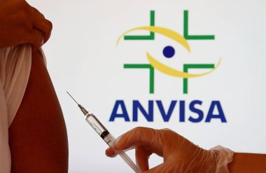 Bahia, Brezilya - 23 Aralık 2020. Kadının omzuna tutulan şırınganın arkasında Anvisa logosu var. Brezilya Sağlık Düzenleme Ajansı (Anvisa) - Covid-19