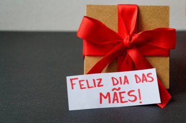 Kırmızı fiyonklu hediye kutusu ve Portekizce 'de' Anneler Günün kutlu olsun 'yazısı (Feliz Dia das Maes).