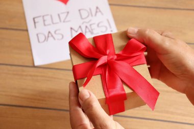 Annemin elinde Portekizce (Feliz Dia das Maes) hediye paketi ve 'Anneler Günün kutlu olsun' kartı var..