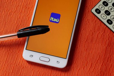 Bahia, Brezilya. 20 Eylül 2020. Itau Bank (Banco Itau) uygulaması turuncu arka planda akıllı telefon ekranında, kalem ve hesap makinesiyle. Brezilya Bankası.