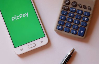 Bahia, Brezilya - 17 Eylül 2020. Akıllı telefon ekranında PicPay uygulaması, beyaz arka planda kalem ve hesap makinesi var. Ödeme kavramı.