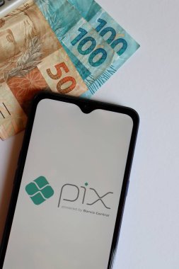 Bahia, Brazil - October 9, 2020: PIX logo on smartphone screen on top of Brazilian Real banknotes. Pix is the new instant payment system from Central Bank of Brazil. Vertical photo.