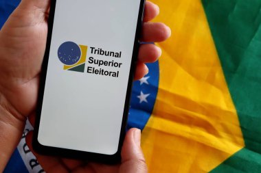 Brezilya - 20 Ekim 2020. Elinde TSE-Yüksek Mahkeme Eleitoral (The Superior Seçim Mahkemesi) logosu ve arkasında Brezilya bayrağı olan akıllı telefon taşıyan kadın. Seçim Adaleti kavramı.