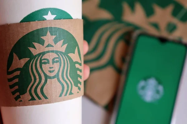 Bahia, Brezilya - 30 Eylül 2020. Starbucks bardağını tutan kadının elinde Starbucks çantası ve arka planda akıllı telefon uygulaması var..