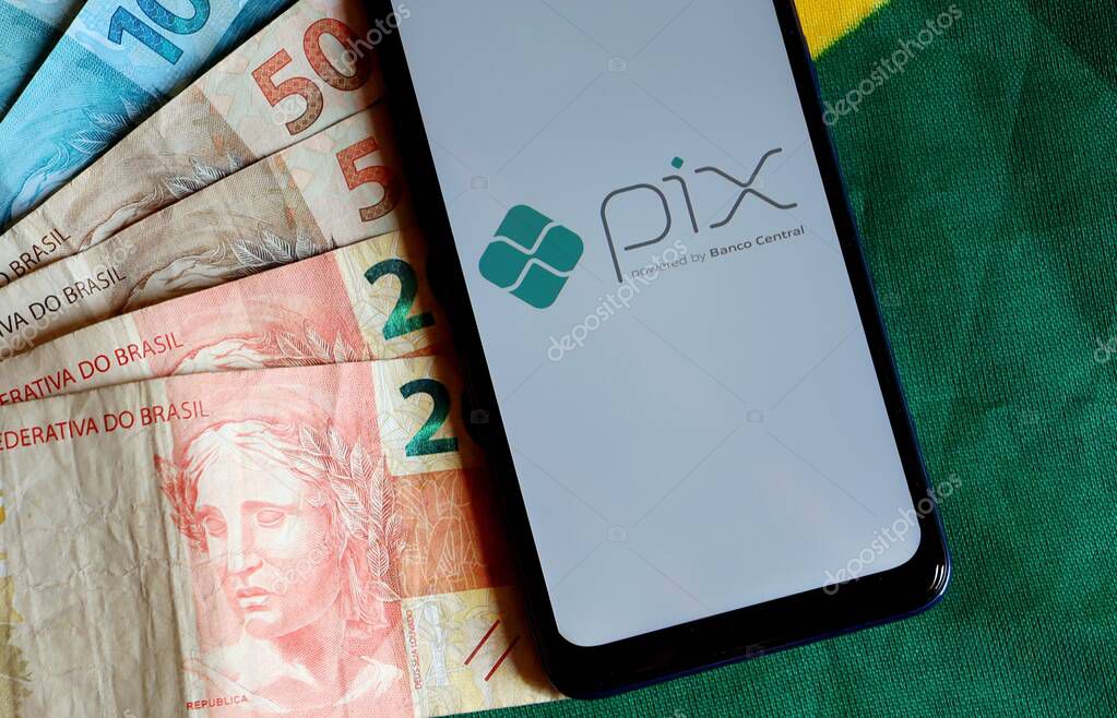 Bahia, Brazil - October 9, 2020: PIX - Powered by Banco Central on smartphone screen and Brazilian money on top of Brazilian flag. Pix is the new instant payment system from Central Bank of Brazil.