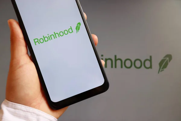 Bahia, Brezilya - 10 Şubat 2021. Robinhood Market logosu olan akıllı telefonu ekranda tutan kadın. Finansal hizmetler. 