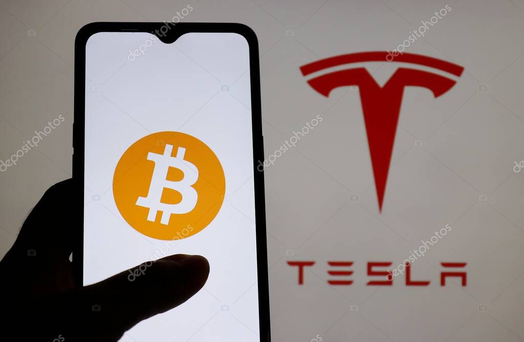Bahia, Brazil - March 26, 2021: Bitcoin logo on smartphone screen with Tesla logo displayed in the background. Tesla cars can be bought in Bitcoin.