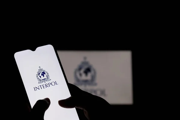 2021年7月26日 巴西巴伊亚州 屏幕上展示了手持带有国际刑警组织标志的智能手机的人 国际刑事警察组织或刑警组织 免版税图库照片