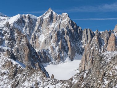 Sivri tepeleri ve tepeleri olan dramatik bir dağ manzarası. Karla kaplı tepeler ve mavi gökyüzü var..
