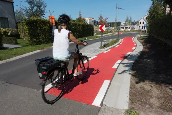 female cyclist cycles on a dedicated cycle lane which is painted red and runs next to a road.She wears a cycle helmet and has a pannier on her bike.