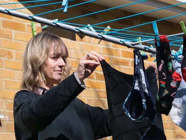A lady hangs out clothes on a rotary drier on a sunny day