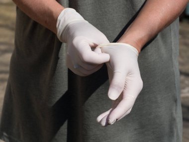 Koronavirüse karşı koruyucu önlem olarak lateks eldivenli bir çift el takılıyor.