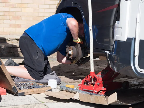 Bir tamirci bir karavan eğlence aracını ele geçirmiş ve tekerleği ve tekerleğin altını sökmüş. Frenleri kontrol ediyor. Trolley kriko, soket takımı görünüyor.
