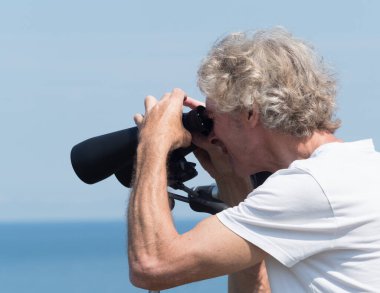 Bempton-Yorkshire-İngiltere-18 Temmuz 2021 - Bir adam arka planda Manfrotto tripodunda desteklenen büyük bir çift skymaster dürbününden bakar.