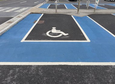 Gri asfalt üzerinde tekerlekli sandalye kullanıcısı işareti olan mavi beyaz bir park yeri.