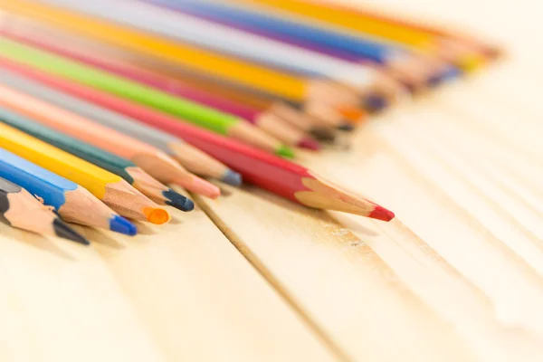 Un crayon rouge se détachant des autres couleurs. sur fond bois — Photo