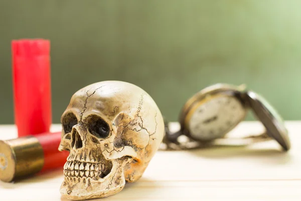 Human skull resting on a wooden floor and a red shotgun shell with antique watches in the background. — Stock Photo, Image