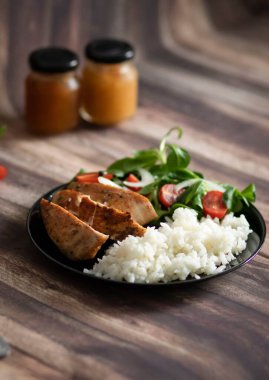 Tavuk göğsü, pilav ve salata. Tüm yiyecekler siyah tabakta