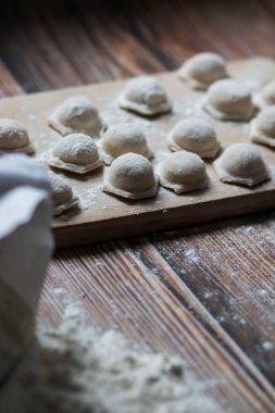 Hamur köftesi pişiriyorum. Çiğ hamur köfteleri tahta bir tahtanın üzerinde yatıyor. Yakınlarda un, merdane ve hamuru bir ahşap zemin üzerinde yatıyor..