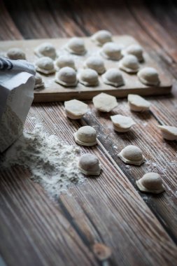 Hamur köftesi pişiriyorum. Çiğ hamur köfteleri tahta bir tahtanın üzerinde yatıyor. Yakınlarda un, merdane ve hamuru bir ahşap zemin üzerinde yatıyor..