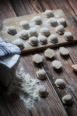 Hamur köftesi pişiriyorum. Çiğ hamur köfteleri tahta bir tahtanın üzerinde yatıyor. Yakınlarda un, merdane ve hamuru bir ahşap zemin üzerinde yatıyor..