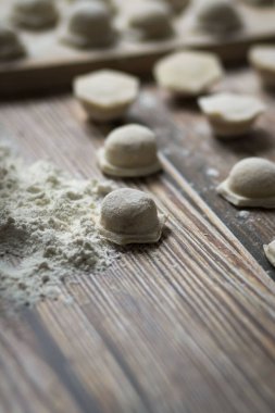 Hamur köftesi pişiriyorum. Çiğ hamur köfteleri tahta bir tahtanın üzerinde yatıyor. Yakınlarda un, merdane ve hamuru bir ahşap zemin üzerinde yatıyor..