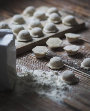 Hamur köftesi pişiriyorum. Çiğ hamur köfteleri tahta bir tahtanın üzerinde yatıyor. Yakınlarda un, merdane ve hamuru bir ahşap zemin üzerinde yatıyor..