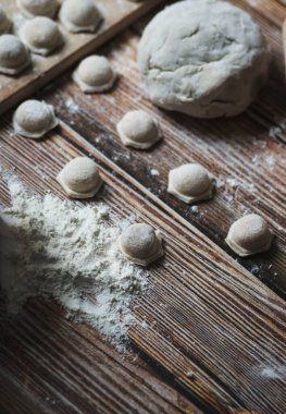 Hamur köftesi pişiriyorum. Çiğ hamur köfteleri tahta bir tahtanın üzerinde yatıyor. Yakınlarda un, merdane ve hamuru bir ahşap zemin üzerinde yatıyor..