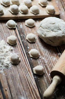 Hamur köftesi pişiriyorum. Çiğ hamur köfteleri tahta bir tahtanın üzerinde yatıyor. Yakınlarda un, merdane ve hamuru bir ahşap zemin üzerinde yatıyor..