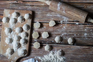 Hamur köftesi pişiriyorum. Çiğ hamur köfteleri tahta bir tahtanın üzerinde yatıyor. Yakınlarda un, merdane ve hamuru bir ahşap zemin üzerinde yatıyor..