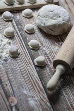 Hamur köftesi pişiriyorum. Çiğ hamur köfteleri tahta bir tahtanın üzerinde yatıyor. Yakınlarda un, merdane ve hamuru bir ahşap zemin üzerinde yatıyor..